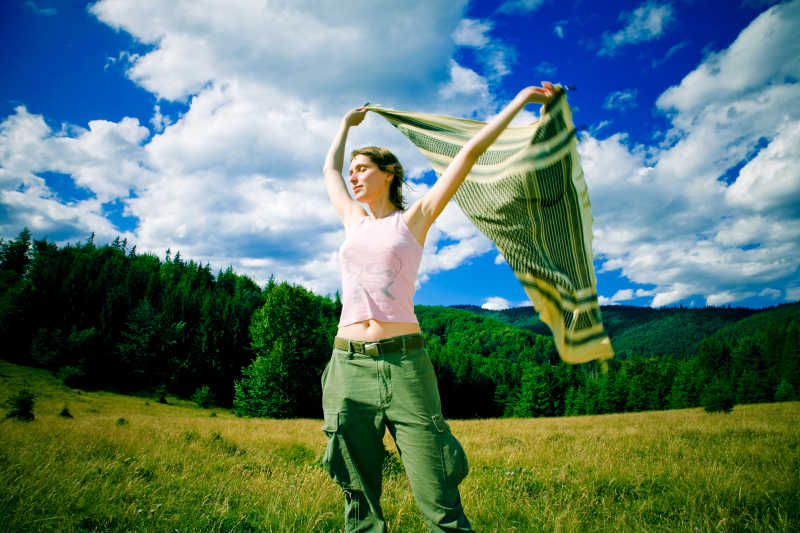 草地上的女子和手里拿着的被风吹动的绿色纱巾